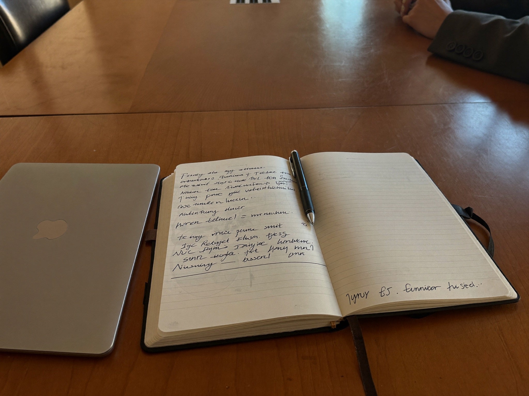 An open paper notebook covered in messy handwritten ink notes on a desk, a phone beside it